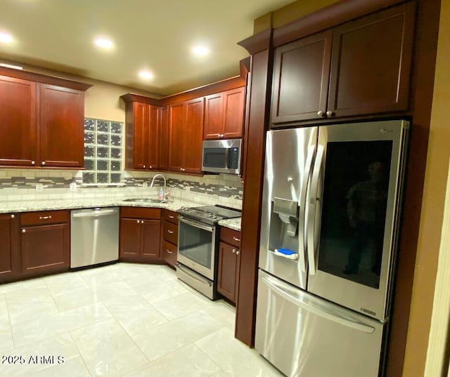 kitchen featuring light stone countertops, a sink, stainless steel appliances, dark brown cabinets, and tasteful backsplash