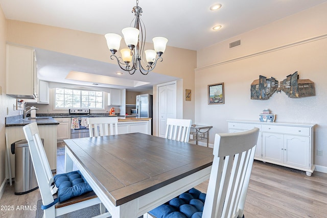 dining area featuring a notable chandelier, a raised ceiling, visible vents, light wood-type flooring, and baseboards