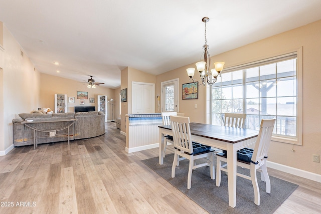 dining room featuring light wood-style floors, vaulted ceiling, baseboards, and ceiling fan with notable chandelier