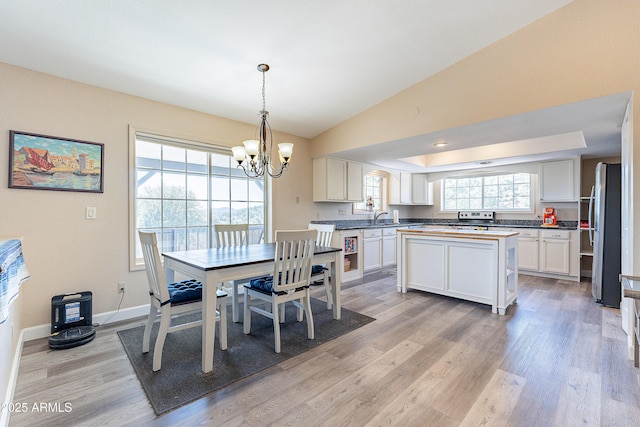 dining room with a tray ceiling, lofted ceiling, an inviting chandelier, light wood-type flooring, and baseboards