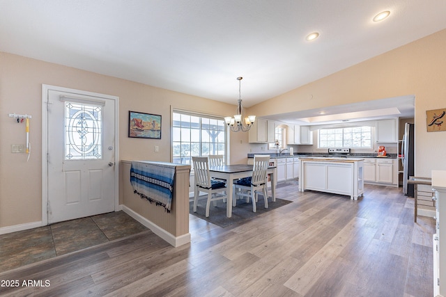 interior space with baseboards, lofted ceiling, an inviting chandelier, light wood-type flooring, and recessed lighting