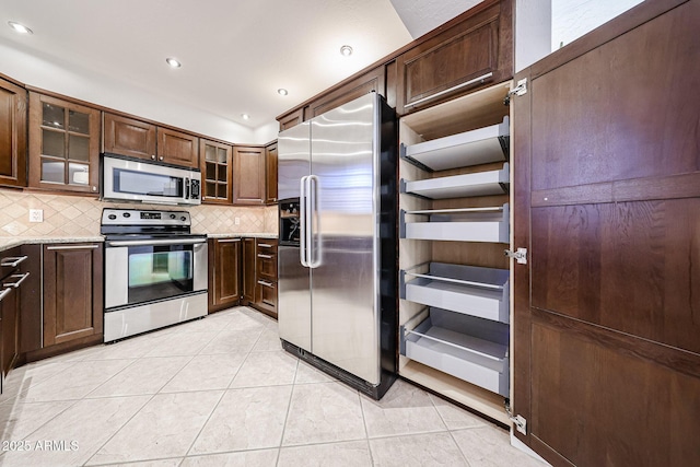 kitchen featuring tasteful backsplash, appliances with stainless steel finishes, light tile patterned floors, and glass insert cabinets