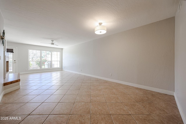 empty room with baseboards, a fireplace with raised hearth, a ceiling fan, a textured ceiling, and light tile patterned flooring