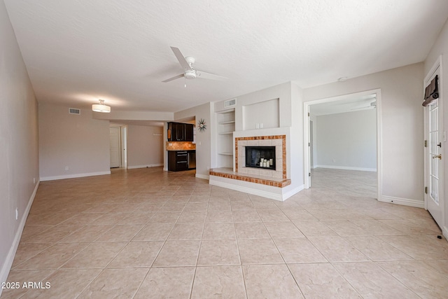 unfurnished living room featuring light tile patterned floors, a ceiling fan, a textured ceiling, built in shelves, and a fireplace