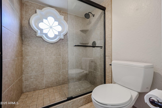 bathroom featuring toilet, tiled shower, and a textured wall