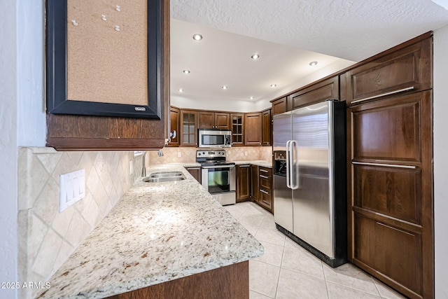 kitchen featuring a sink, light tile patterned floors, light stone counters, stainless steel appliances, and glass insert cabinets