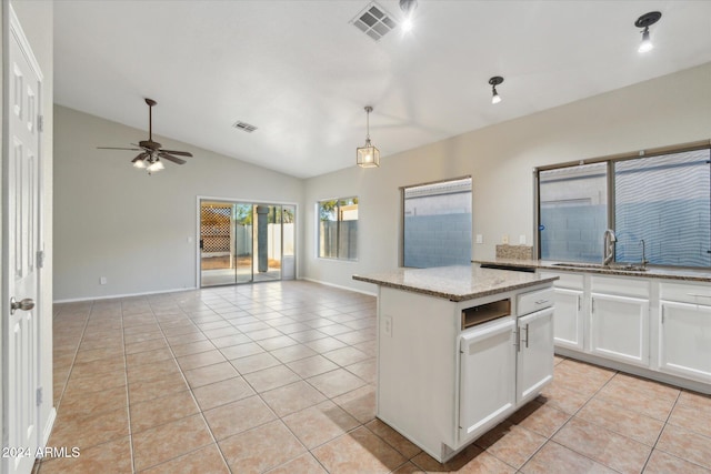 kitchen featuring a center island, vaulted ceiling, light tile patterned floors, light stone counters, and white cabinetry