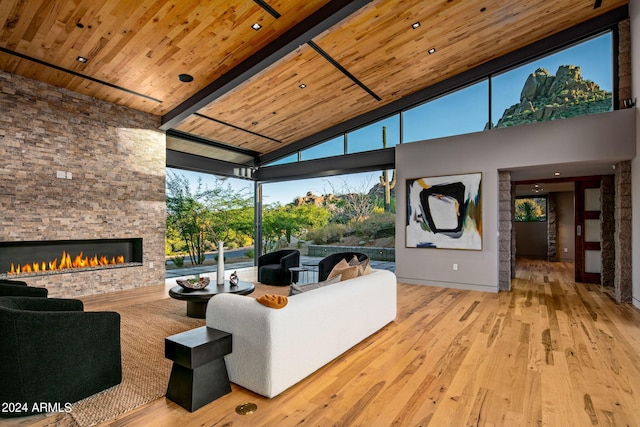 living room featuring beamed ceiling, wooden ceiling, light hardwood / wood-style flooring, a fireplace, and high vaulted ceiling