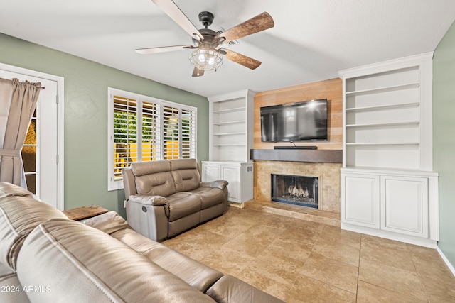 tiled living room featuring ceiling fan, built in shelves, and a high end fireplace