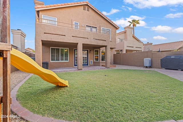 back of property with a playground, a yard, a balcony, and a patio area