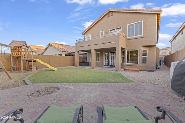 back of house featuring a playground, a balcony, a lawn, and a patio