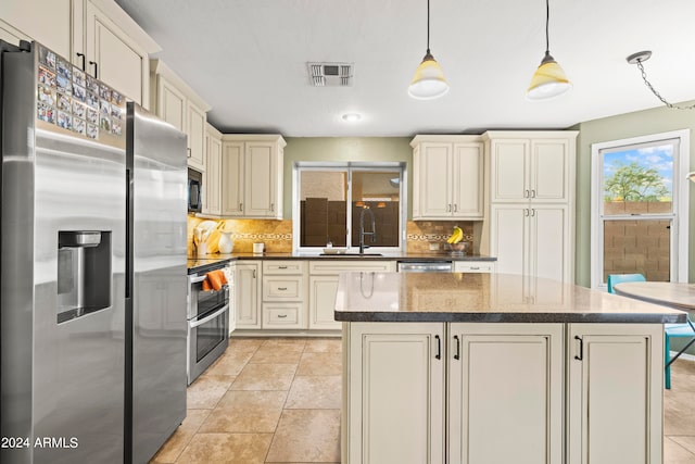 kitchen with tasteful backsplash, sink, hanging light fixtures, appliances with stainless steel finishes, and cream cabinets