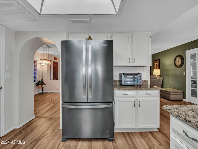 kitchen featuring white cabinets, hanging light fixtures, stainless steel refrigerator, dark stone counters, and light hardwood / wood-style floors