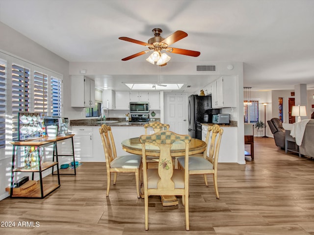 dining area with a skylight, ceiling fan, sink, and light hardwood / wood-style flooring