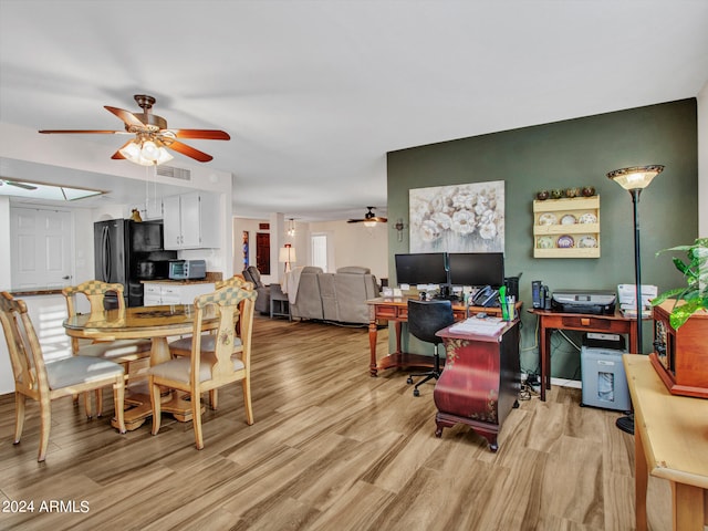 dining space with ceiling fan, a skylight, and light wood-type flooring