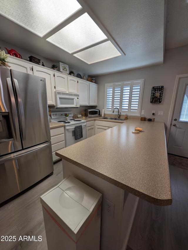 kitchen featuring white appliances, wood finished floors, a peninsula, a sink, and white cabinetry