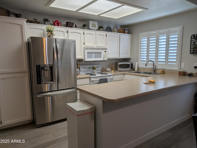 kitchen with a sink, white appliances, a peninsula, and white cabinets