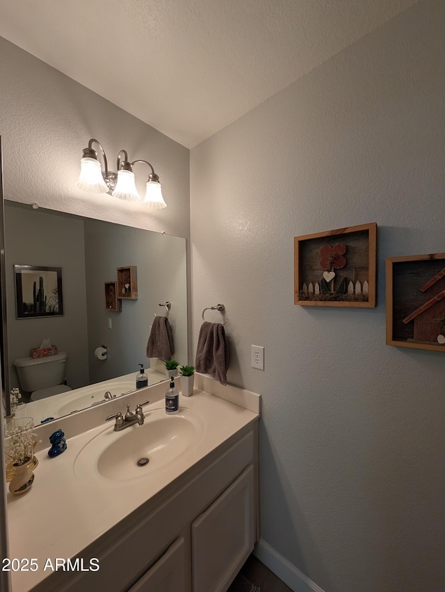 half bath with toilet, vanity, and a textured wall