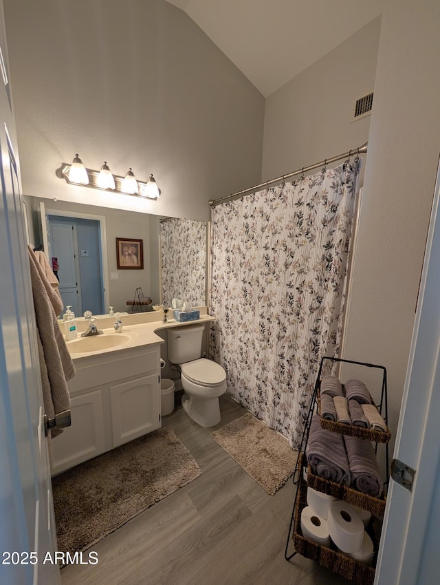 bathroom featuring visible vents, toilet, wood finished floors, vanity, and vaulted ceiling