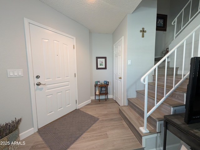 entryway featuring stairway, light wood-style flooring, baseboards, and a textured ceiling