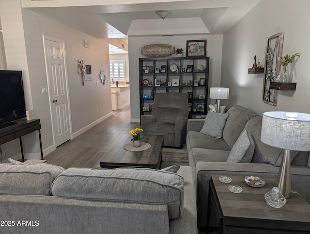 living room featuring visible vents, a raised ceiling, baseboards, and wood finished floors