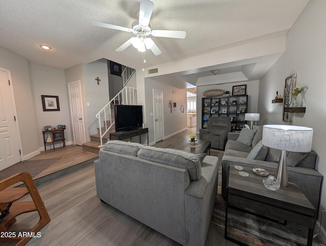 living room with a textured ceiling, stairs, a ceiling fan, and wood finished floors