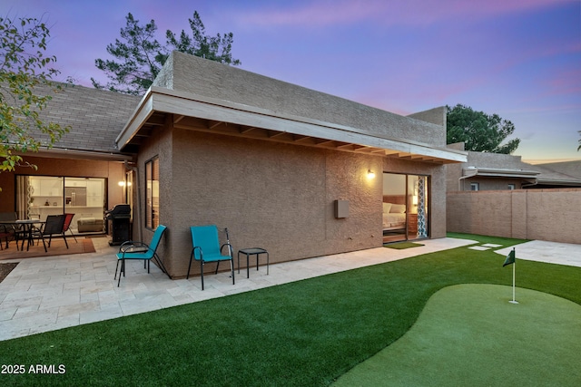 back of property at dusk featuring a patio area, fence, and stucco siding