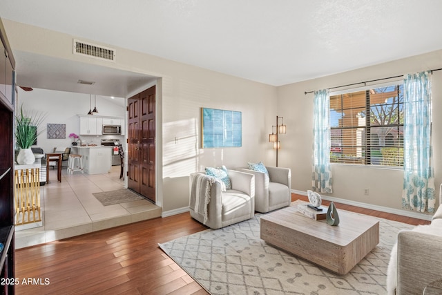 living area featuring visible vents, light wood-style flooring, and baseboards