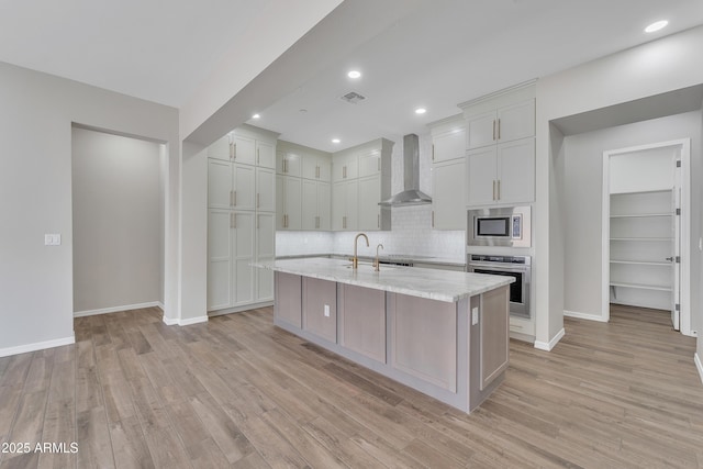 kitchen featuring appliances with stainless steel finishes, light wood finished floors, and wall chimney exhaust hood