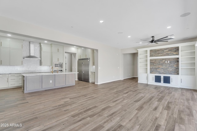 kitchen with open floor plan, light countertops, wall chimney exhaust hood, and built in appliances