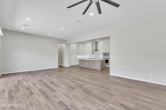 unfurnished living room with light wood finished floors, recessed lighting, a ceiling fan, a sink, and baseboards