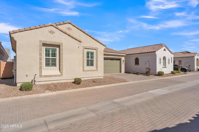 mediterranean / spanish-style home with a garage, a tiled roof, decorative driveway, and stucco siding