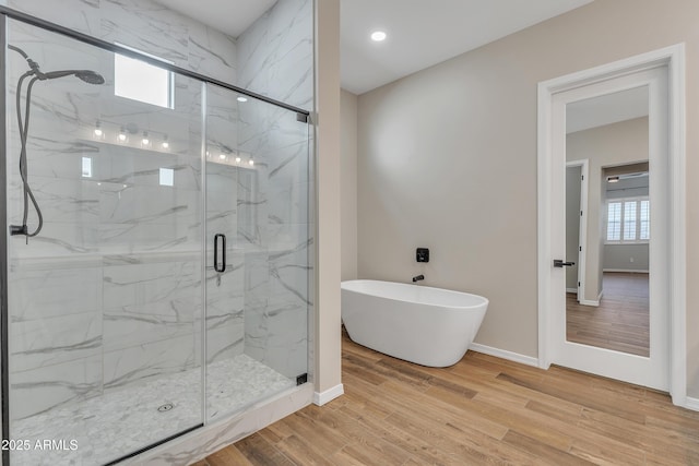 full bath featuring a freestanding tub, baseboards, a marble finish shower, and wood finished floors