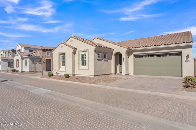 mediterranean / spanish home featuring a residential view, a tiled roof, an attached garage, decorative driveway, and stucco siding