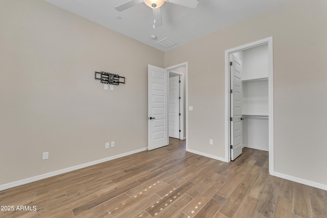 unfurnished bedroom with baseboards, ceiling fan, a walk in closet, light wood-type flooring, and a closet