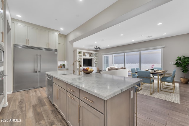 kitchen with stainless steel appliances, a center island with sink, a sink, and light wood finished floors