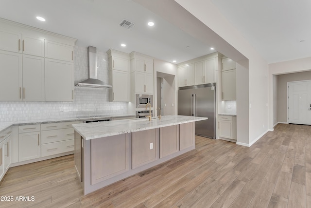 kitchen with wall chimney range hood, visible vents, backsplash, and built in appliances