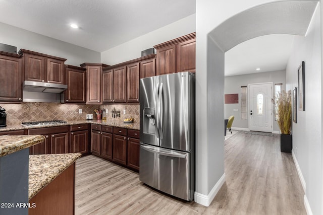 kitchen with backsplash, light wood-type flooring, appliances with stainless steel finishes, dark brown cabinets, and light stone counters