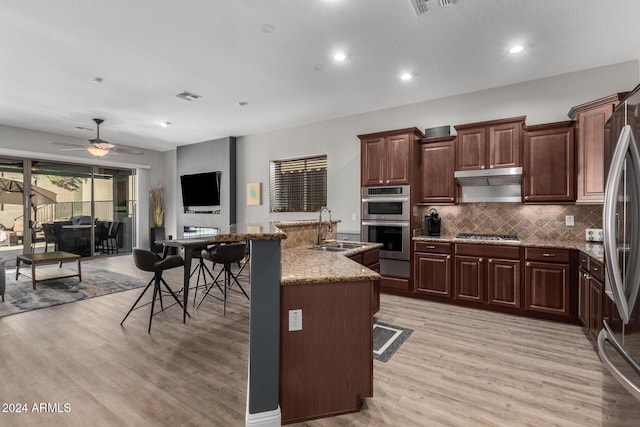 kitchen with ceiling fan, sink, stainless steel appliances, a kitchen breakfast bar, and an island with sink