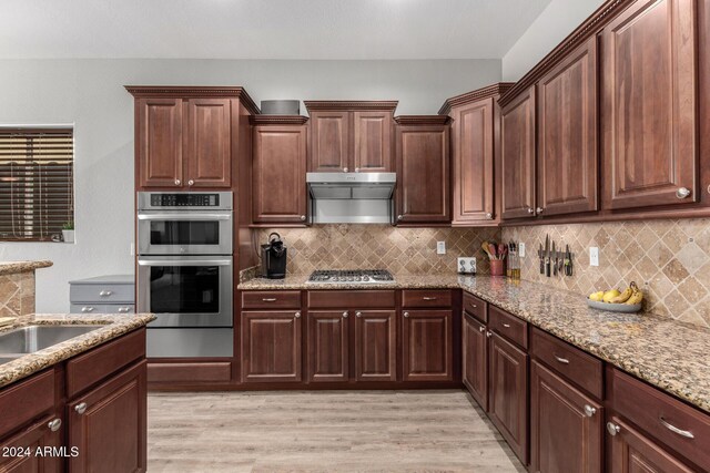 kitchen with backsplash, light hardwood / wood-style floors, light stone counters, and stainless steel appliances