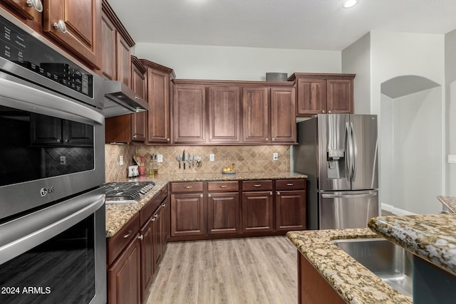 kitchen featuring light stone countertops, sink, stainless steel appliances, tasteful backsplash, and light hardwood / wood-style flooring