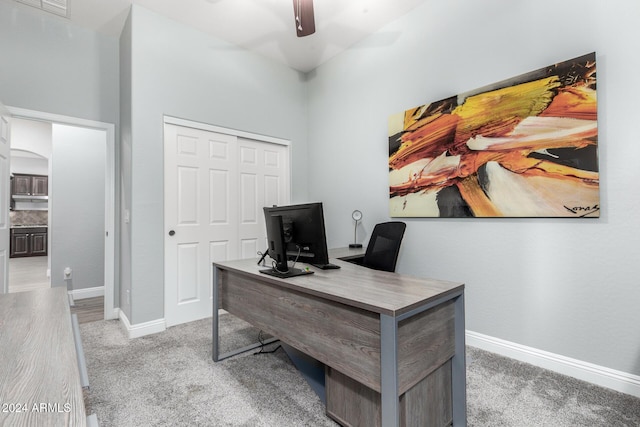 carpeted office space with a towering ceiling and ceiling fan