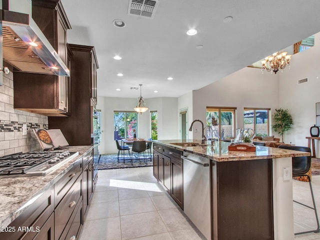 kitchen featuring sink, decorative light fixtures, appliances with stainless steel finishes, an island with sink, and exhaust hood