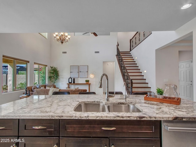 kitchen featuring an inviting chandelier, sink, dark brown cabinets, and light stone countertops