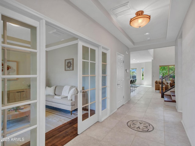 hall featuring french doors, a tray ceiling, and light tile patterned flooring