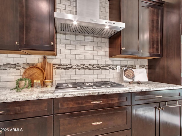 kitchen with wall chimney exhaust hood, light stone counters, dark brown cabinetry, tasteful backsplash, and stainless steel gas stovetop