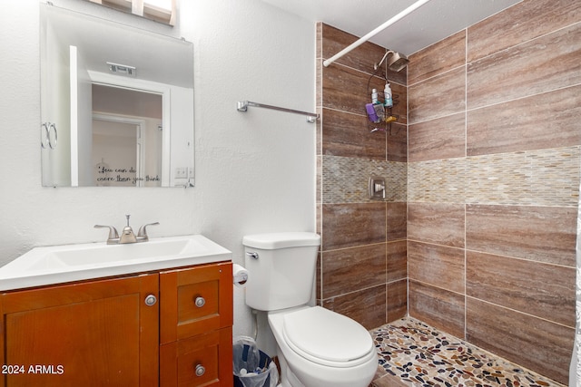 bathroom with toilet, a tile shower, and vanity