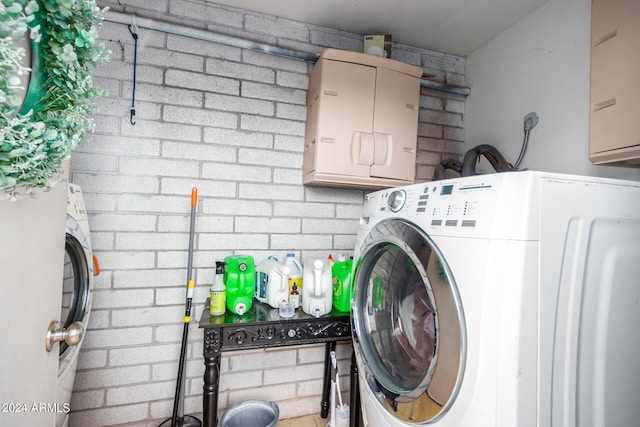 clothes washing area with washer / clothes dryer, brick wall, and cabinets