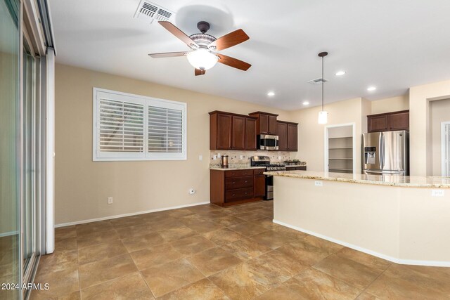 kitchen featuring tasteful backsplash, stainless steel appliances, hanging light fixtures, a ceiling fan, and light stone countertops