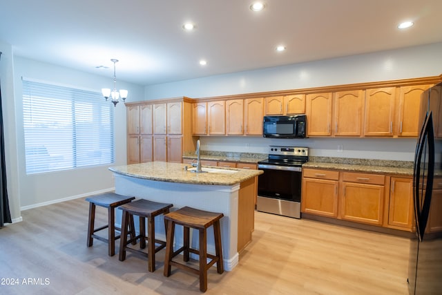 kitchen featuring pendant lighting, light hardwood / wood-style flooring, black appliances, and a center island with sink